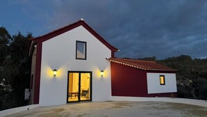 Un edificio de dos pisos con fachada roja y blanca, una puerta de entrada de vidrio grande y dos ventanas pequeñas en el piso superior.