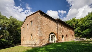 Ein Gebäude aus Stein mit einem großen Bogenportal, einer kleinen Veranda mit Sitzgelegenheiten und einer Rasenfläche davor.