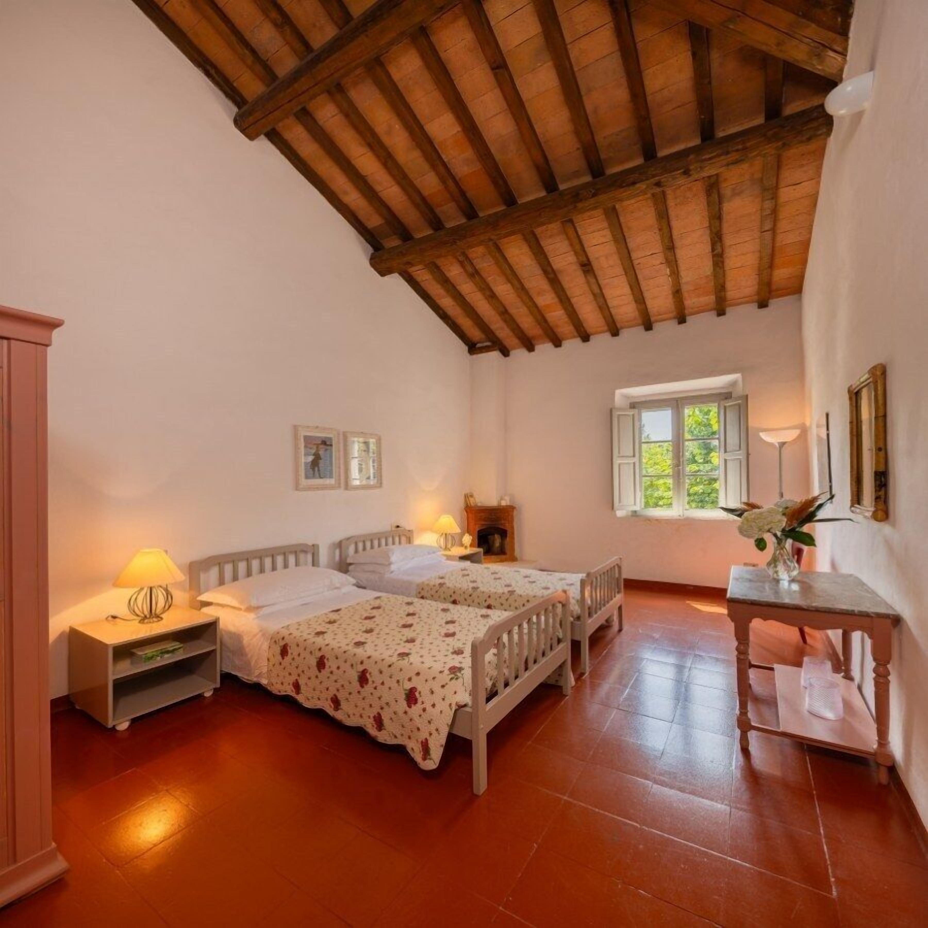 Un dormitorio con dos camas individuales, techo de madera, ventana con vistas y una pequeña mesa con un florero.