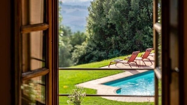 Ein Fenster mit Blick auf einen Swimmingpool, eine Rasenfläche und eine bewaldete Landschaft.