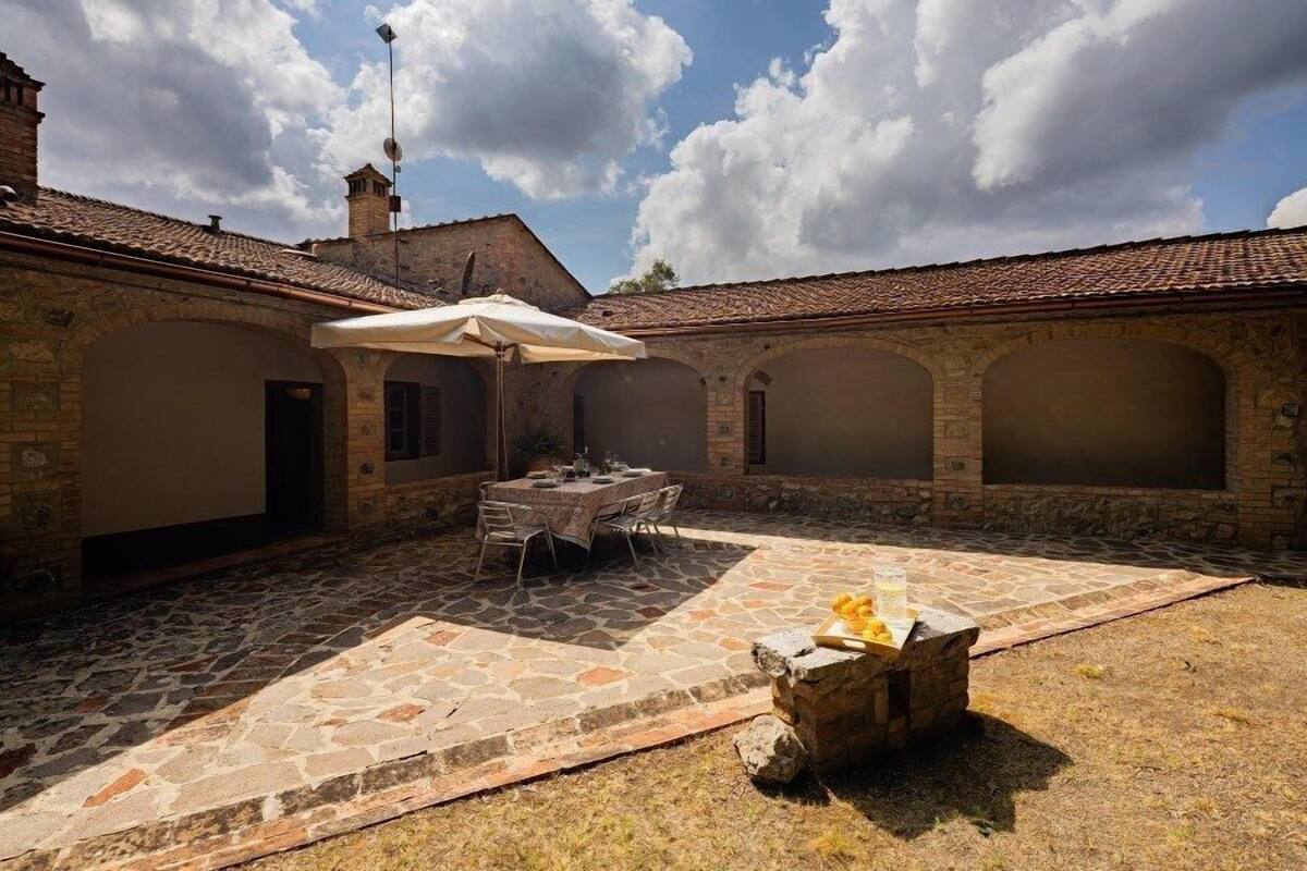 A courtyard with a stone floor, a table with chairs, and a stone fire pit.