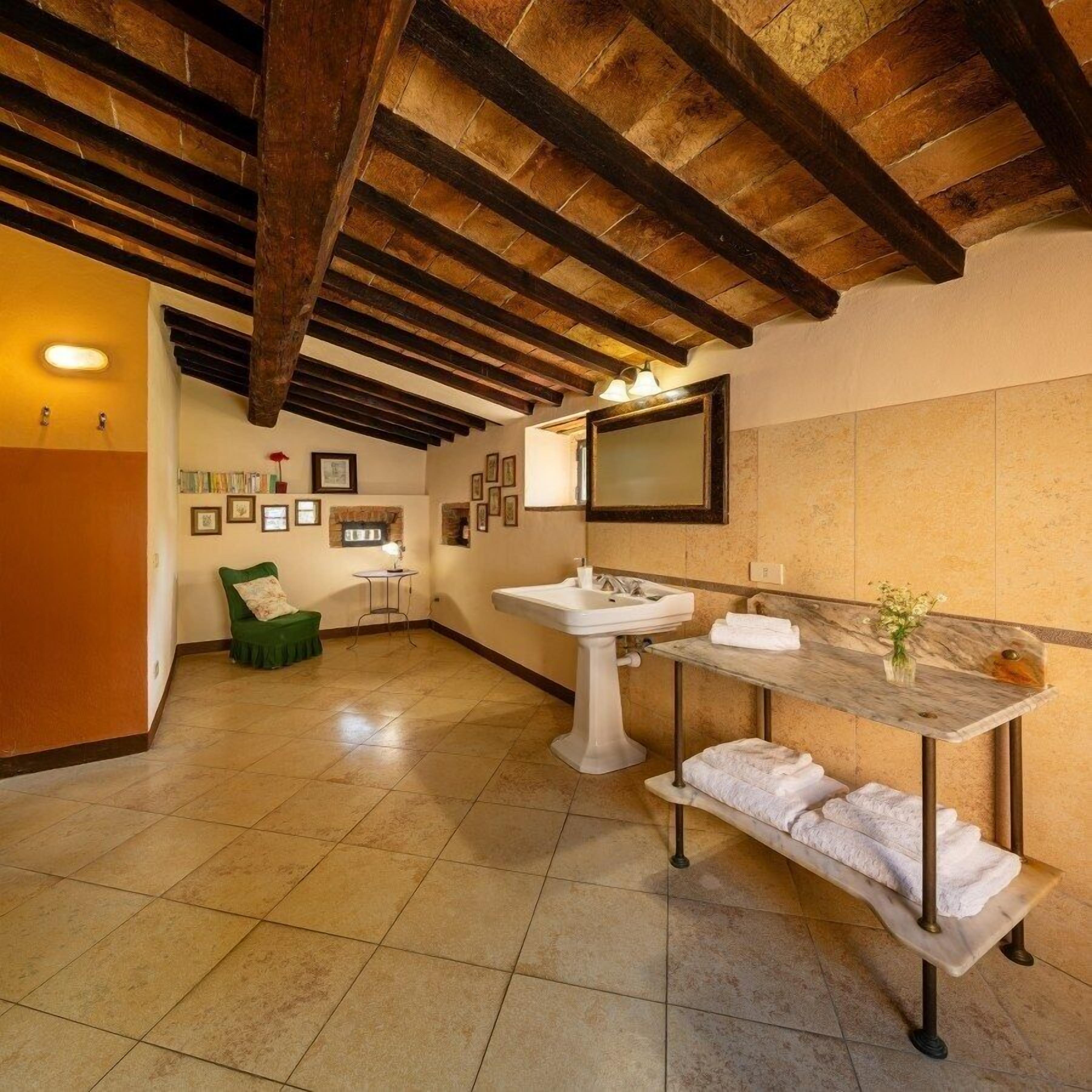 Un baño con techo de madera, un lavamanos, un espejo y una silla verde.