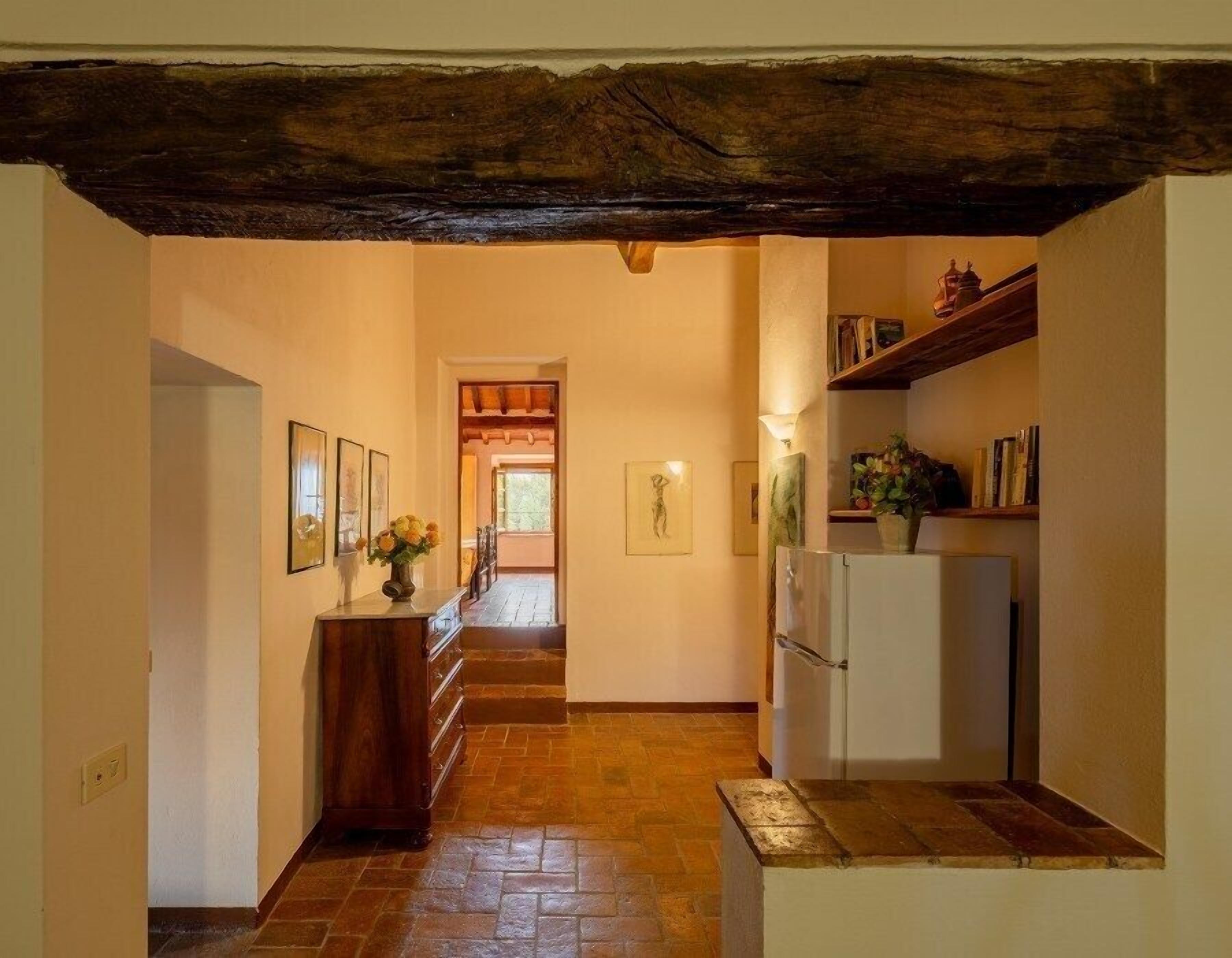 A hallway with a wooden ceiling, a staircase, a refrigerator, and framed artwork on the walls.