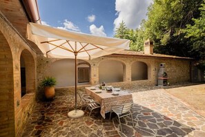 Eine Terrasse im Freien mit einem Essplatz, umgeben von Steinmauern und einem großen Sonnenschirm.