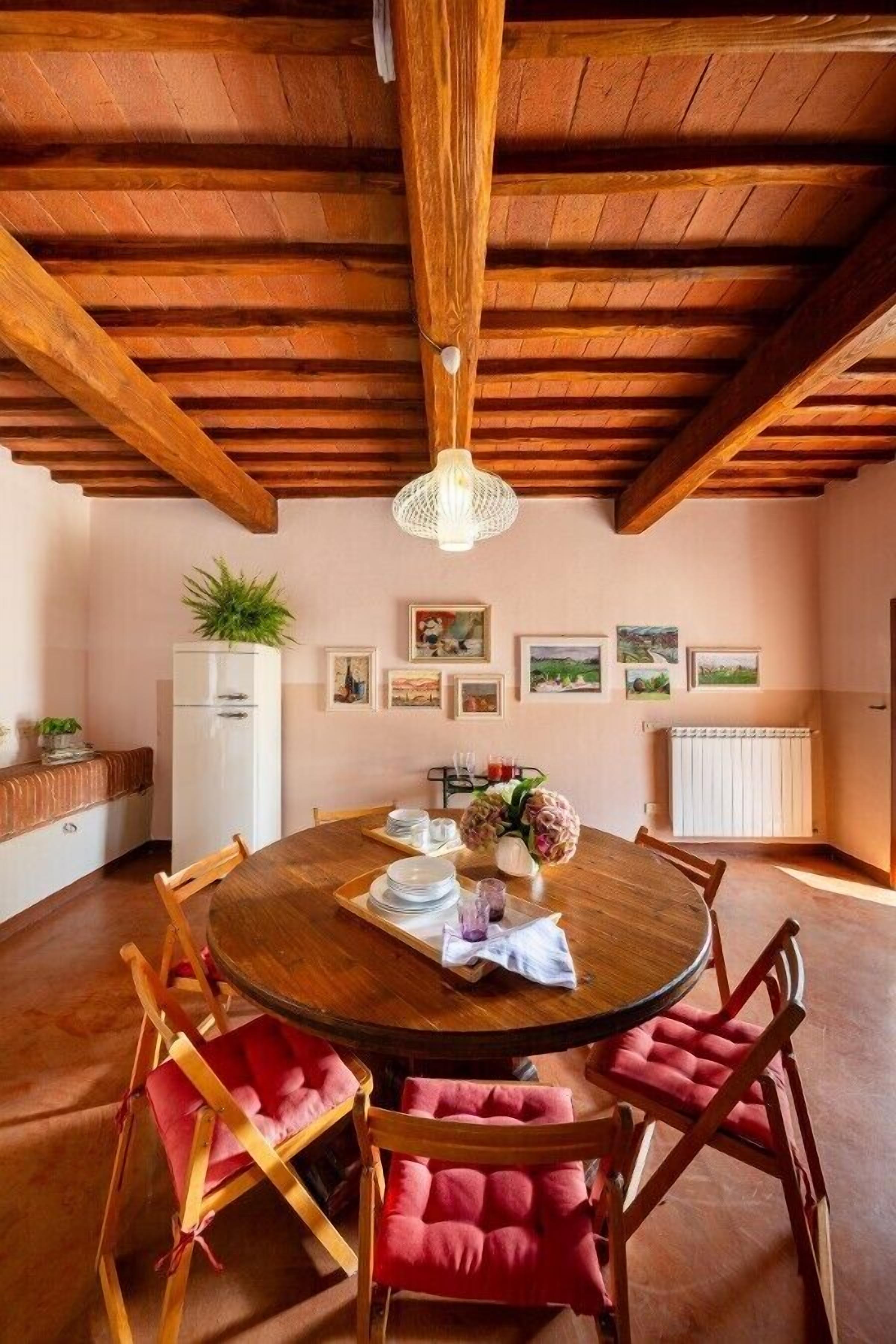 Un comedor con mesa de madera, sillas rojas acolchadas, un refrigerador blanco y una lámpara colgante.