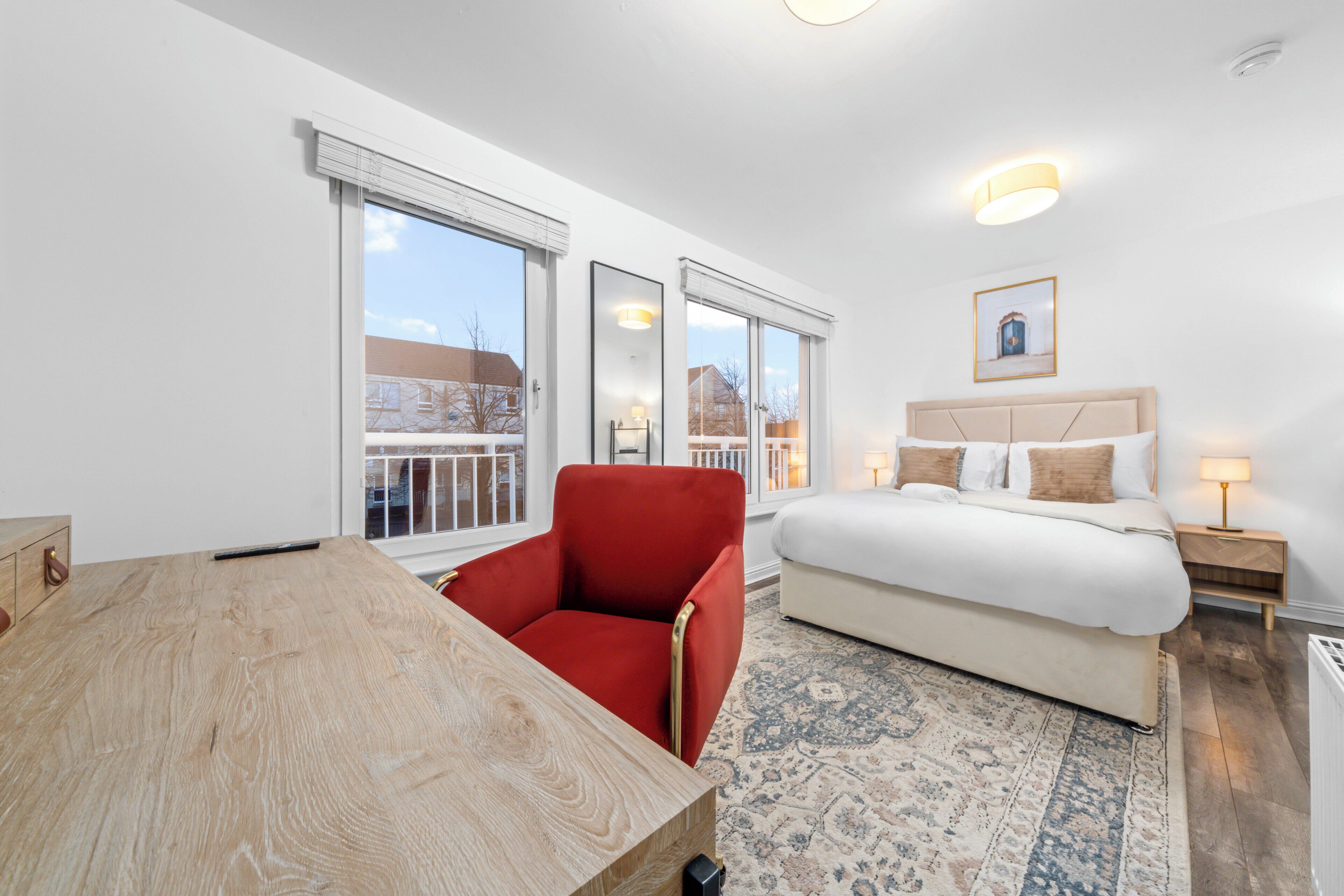 A modern bedroom with a large bed, a red chair, a wooden table, and a view of the outside.