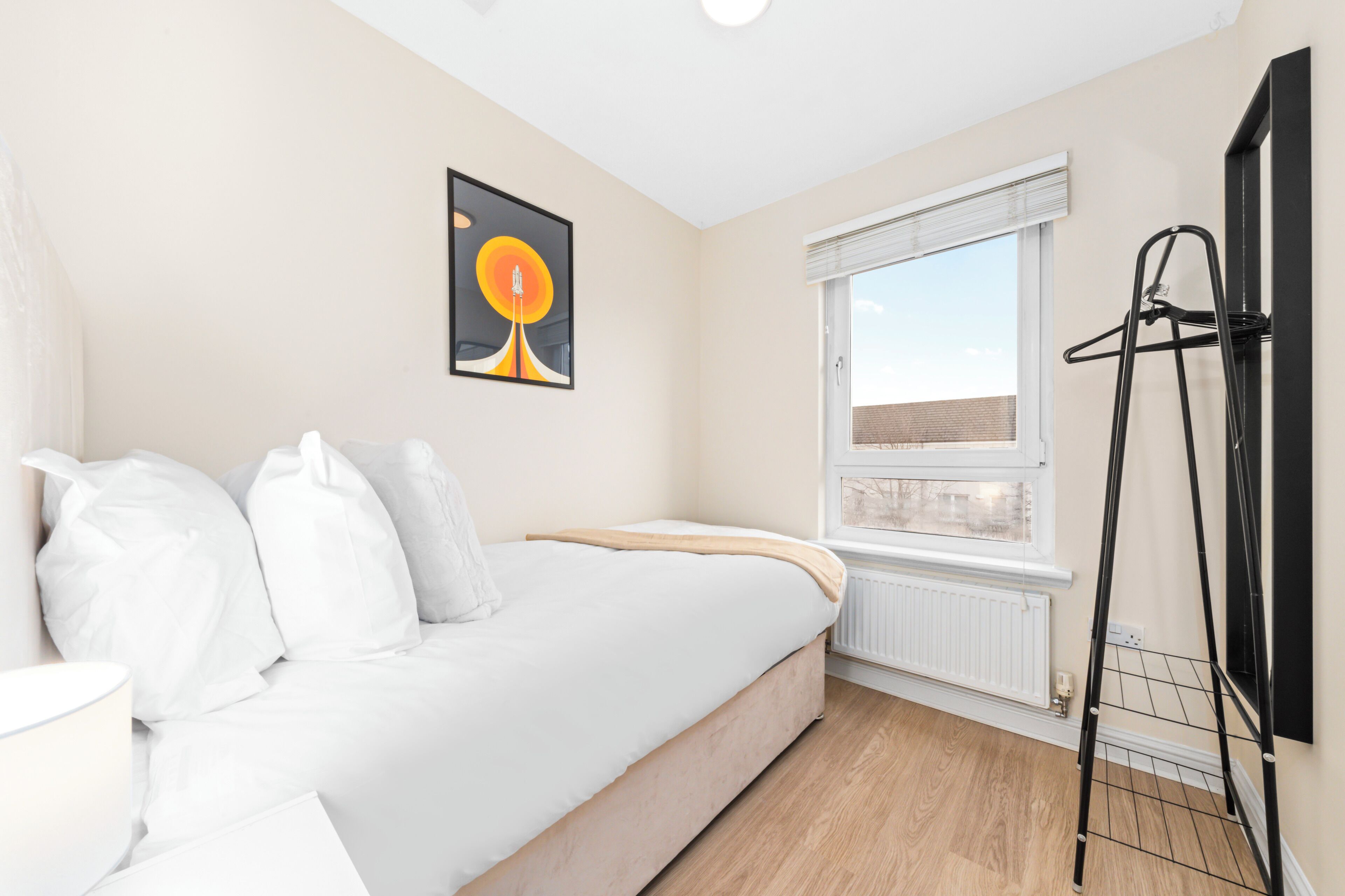 A bedroom with a bed, a radiator, a window, and a black hanger rack.