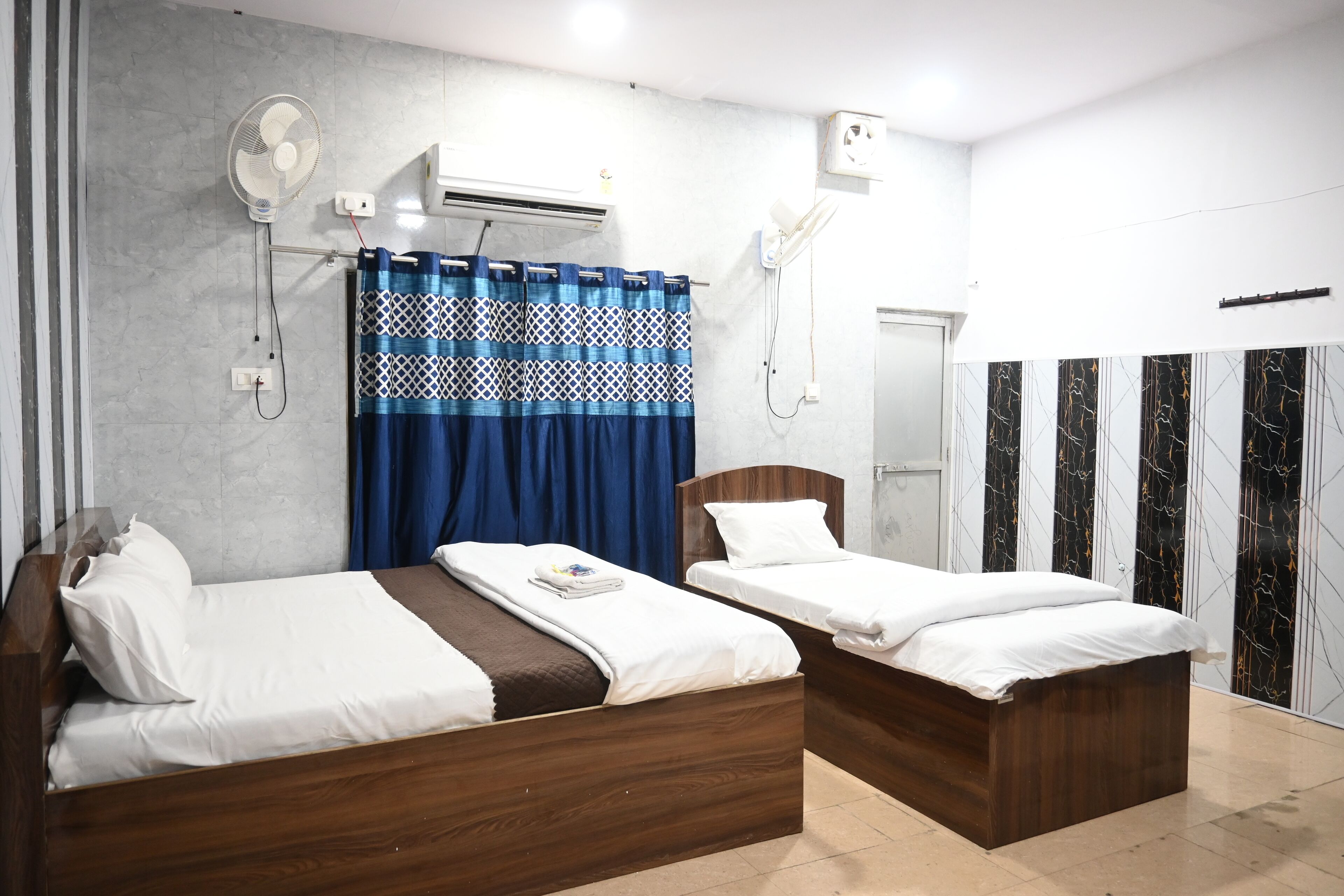 A hotel room with two wooden beds, a blue curtain, and a marble-patterned wall.