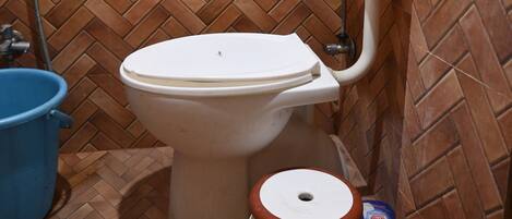 A bathroom with a herringbone patterned tile wall, a white toilet, a blue basin, and a small trash bin.
