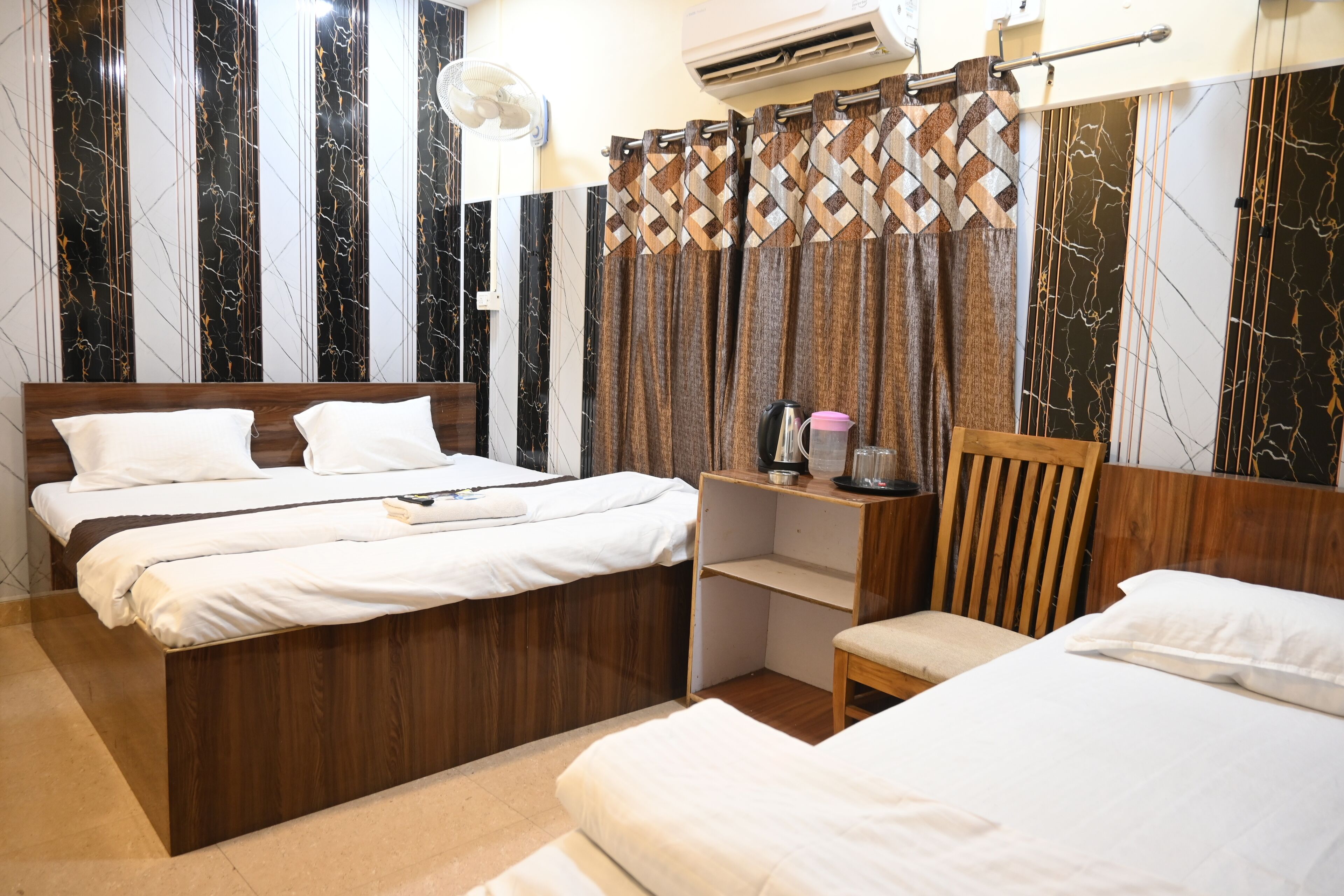 A hotel room with two beds, a wooden desk, a chair, and a wall-mounted air conditioner.