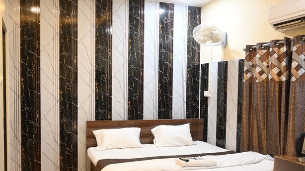 Una habitación de hotel moderna con una cama grande, cabecero de madera y paredes con diseño de mármol.