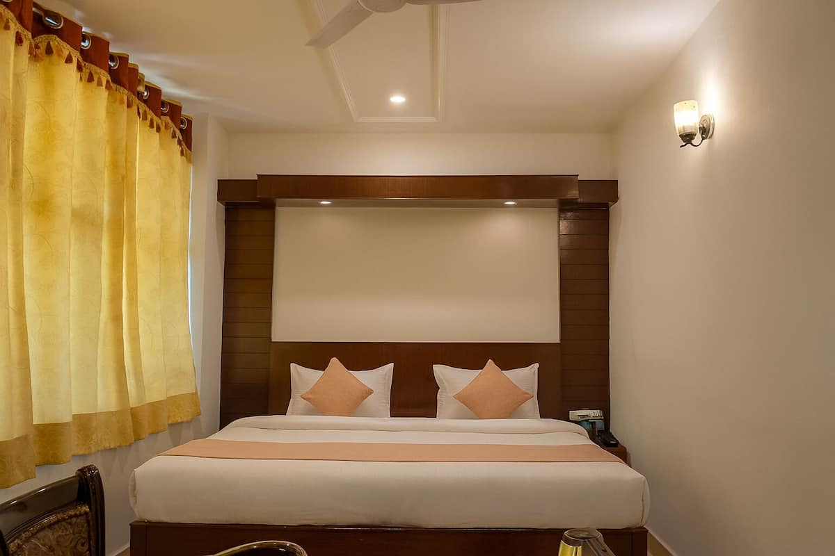 A hotel room with a large bed, a headboard, a nightstand, and a wall-mounted light fixture.