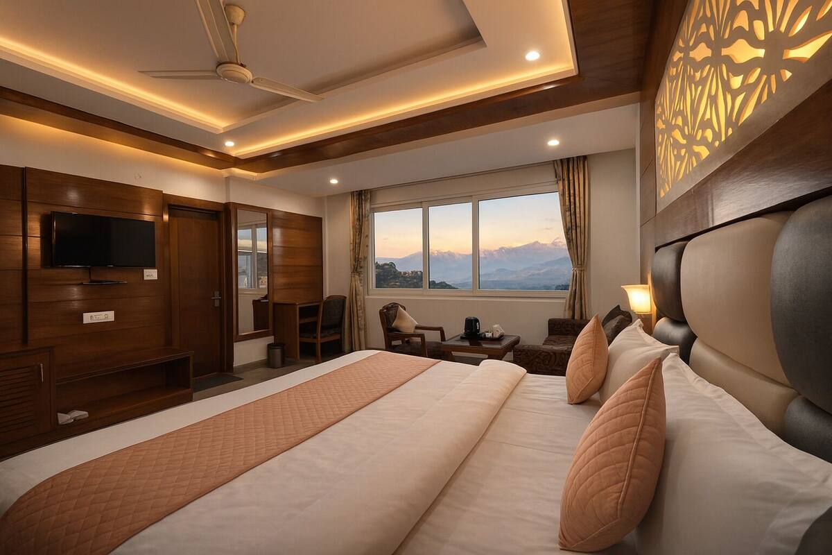 A hotel room with a large bed, a TV, a desk, and a view of mountains through the window.