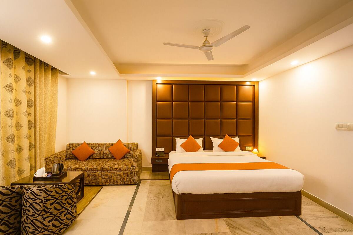 A hotel room with a bed, a sofa, a nightstand, a ceiling fan, and patterned curtains.