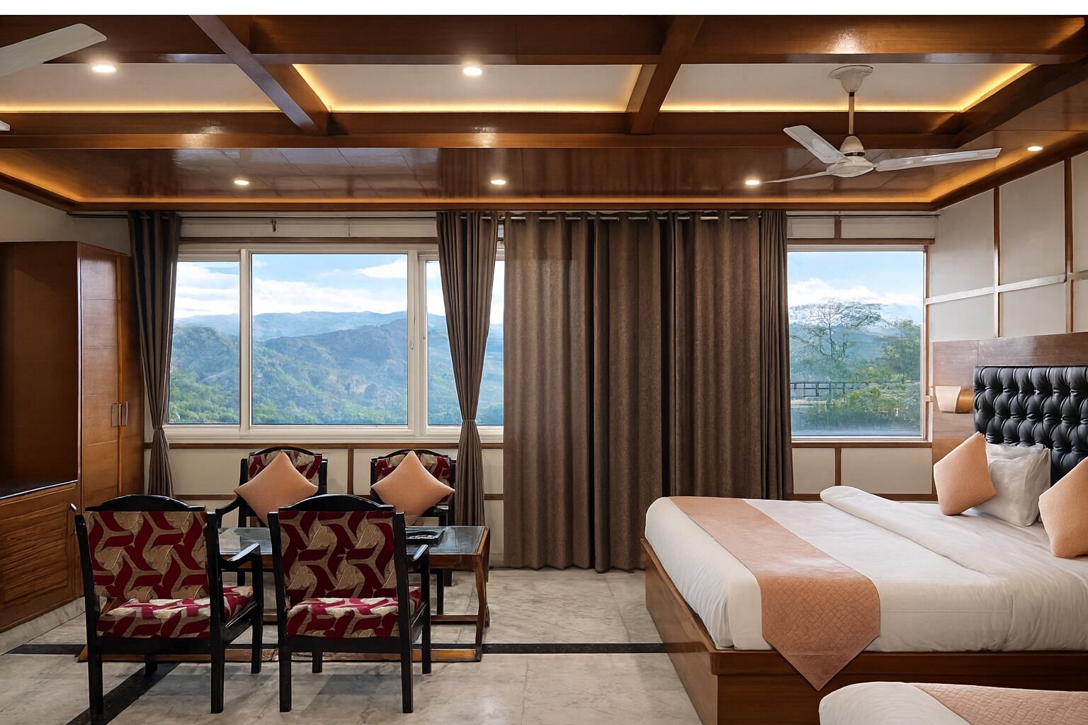 A hotel room with a bed, a desk with chairs, and a view of mountains.
