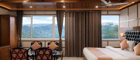 A hotel room with a bed, a desk with chairs, and a view of mountains.