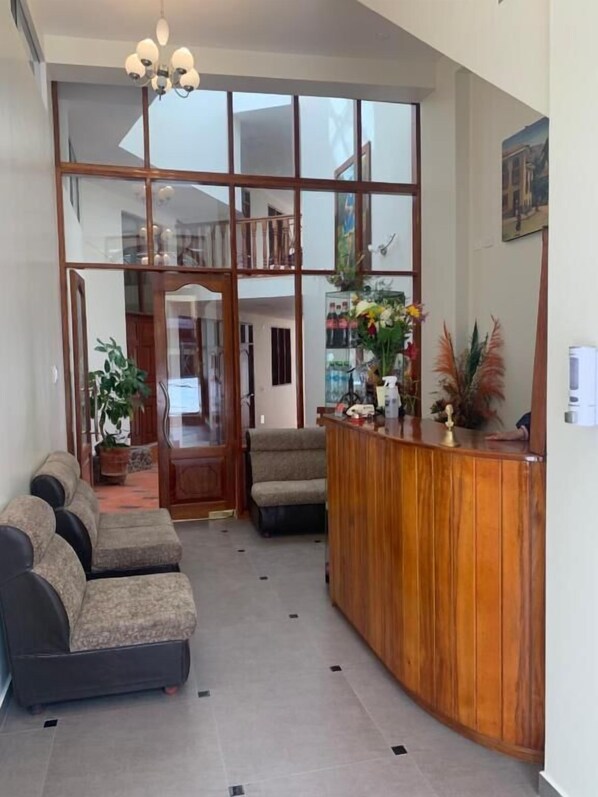 Un espace d’accueil comprenant un comptoir de réception en bois, un canapé et une plante en pot.