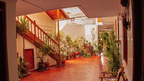 A spacious indoor area with a wooden staircase, potted plants, and a red-tiled floor. - Hotel El Chasqui (Ollantaytambo)