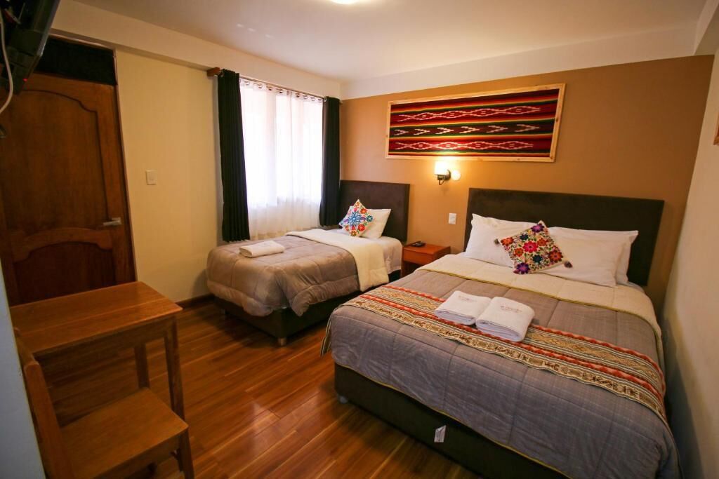 A hotel room with two beds, wooden flooring, a desk, and a door.