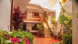 A courtyard with a staircase leading to a balcony, surrounded by potted plants and flowers. - Hotel El Chasqui (Ollantaytambo)