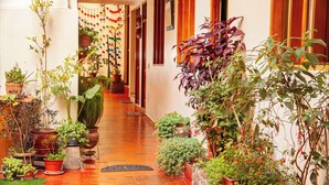 A corridor with potted plants and a brick floor. - Hotel El Chasqui (Ollantaytambo)