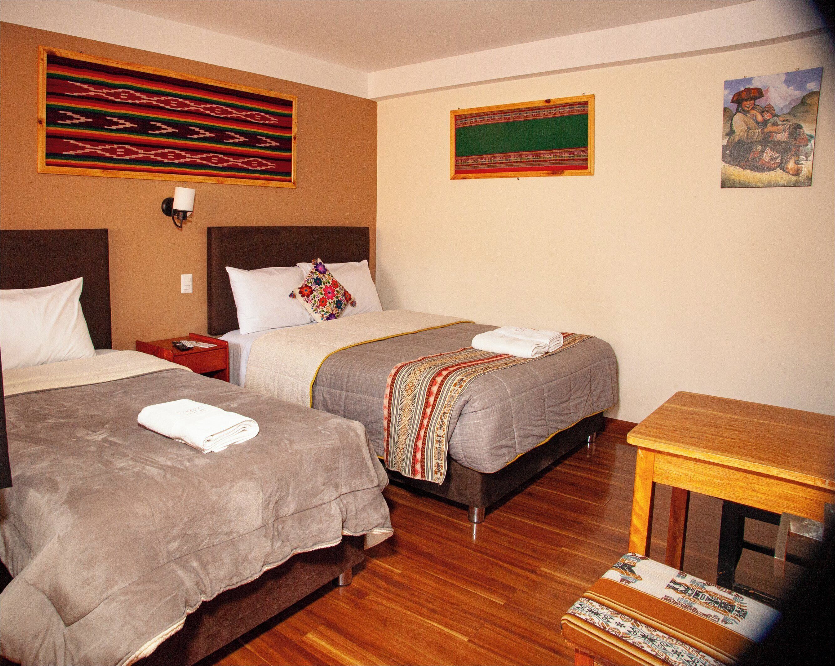 A hotel room with two beds, wooden flooring, and a small wooden table.
