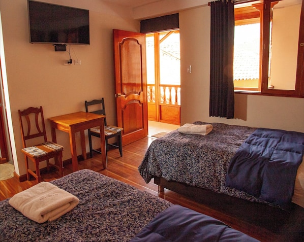 Une chambre d’hôtel avec deux lits, un bureau, une chaise et un téléviseur fixé au mur.