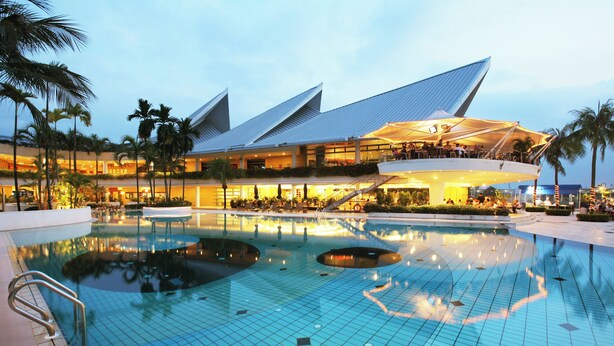 Ein Hotel mit Schwimmbad, Palmen und einem markanten, modernen Gebäude mit einzigartigem Dachdesign.
