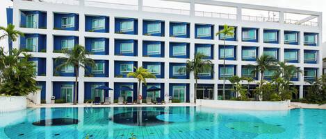 Um hotel moderno com uma piscina grande, várias varandas e palmeiras.