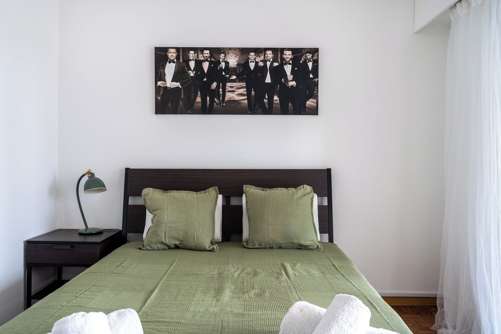 Ein Schlafzimmer mit einem Bett, Kissen, einem Nachttisch, einer Lampe und einem gerahmten Bild an der Wand.