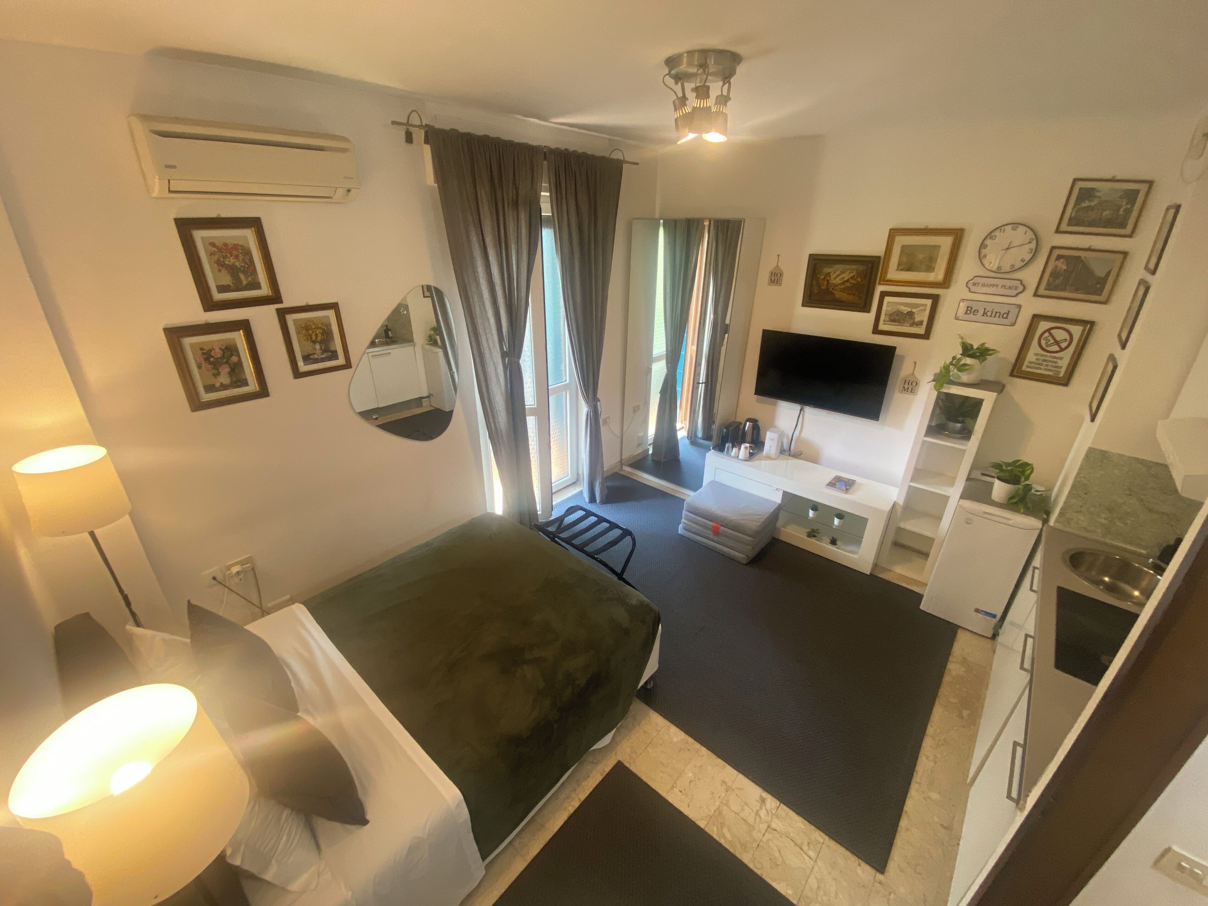A hotel room with a bed, a desk, a TV, a mirror, and a kitchenette.