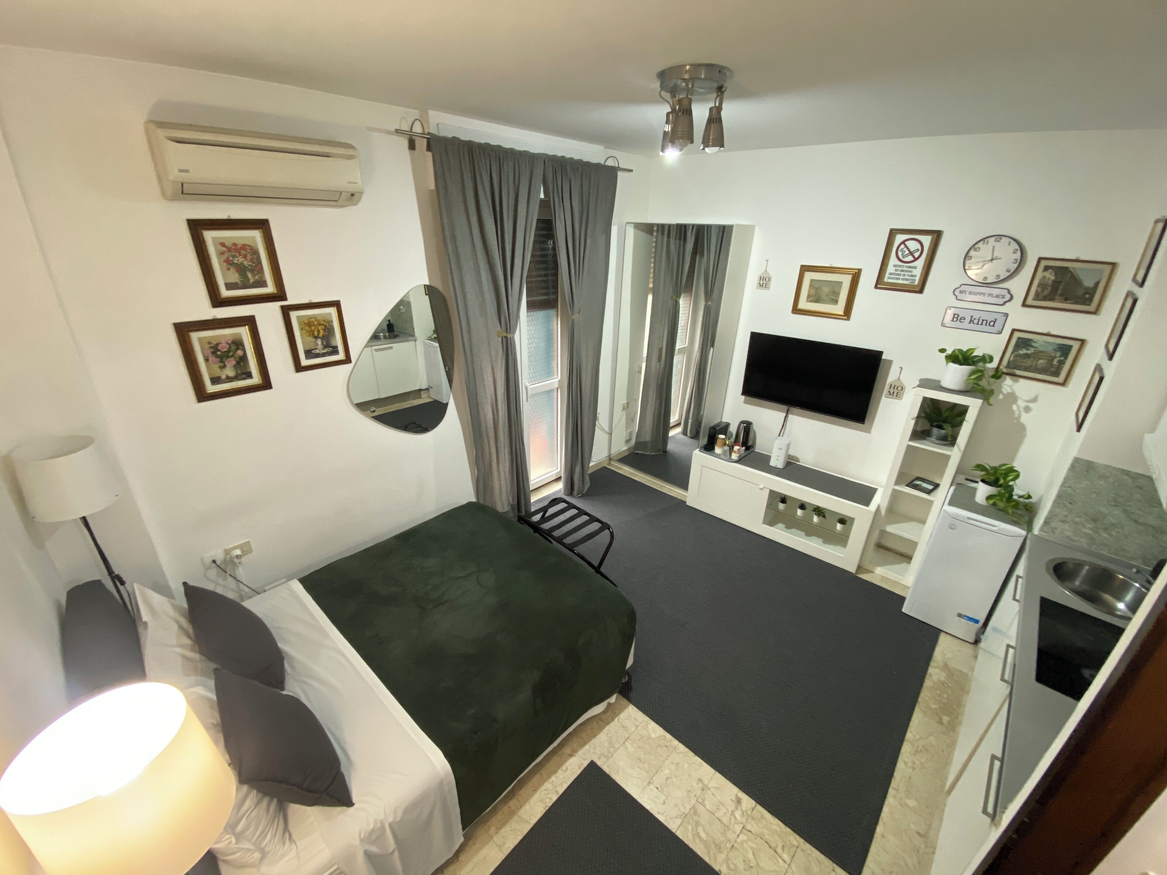 A compact hotel room with a bed, a desk, a TV, and a kitchenette.