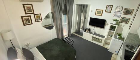 A compact hotel room with a bed, a desk, a TV, and a kitchenette.