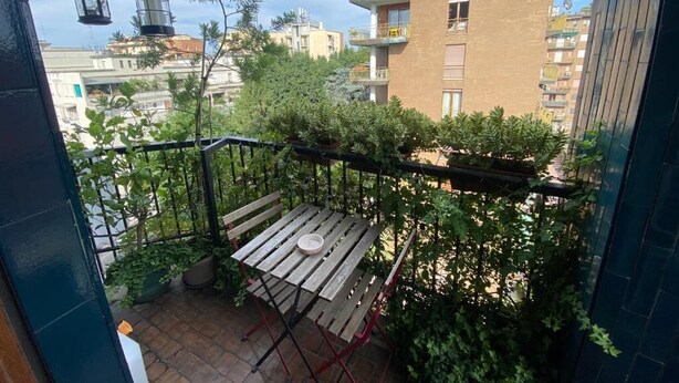 A balcony with a wooden table and chairs, surrounded by greenery and overlooking a residential area with multiple buildings. - Short Rent Milano Porta Vittoria (Milan)