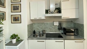 A modern kitchen with white cabinets, a built-in microwave, and a sink. There are framed pictures on the wall and a potted plant on the counter. - Short Rent Milano Porta Vittoria (Milan)
