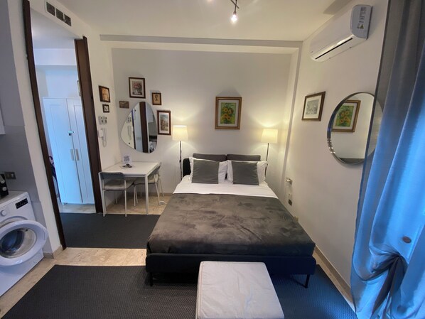 A hotel room with a bed, bedside table, chair, desk, and a washing machine. - Short Rent Milano Porta Vittoria (Milan)
