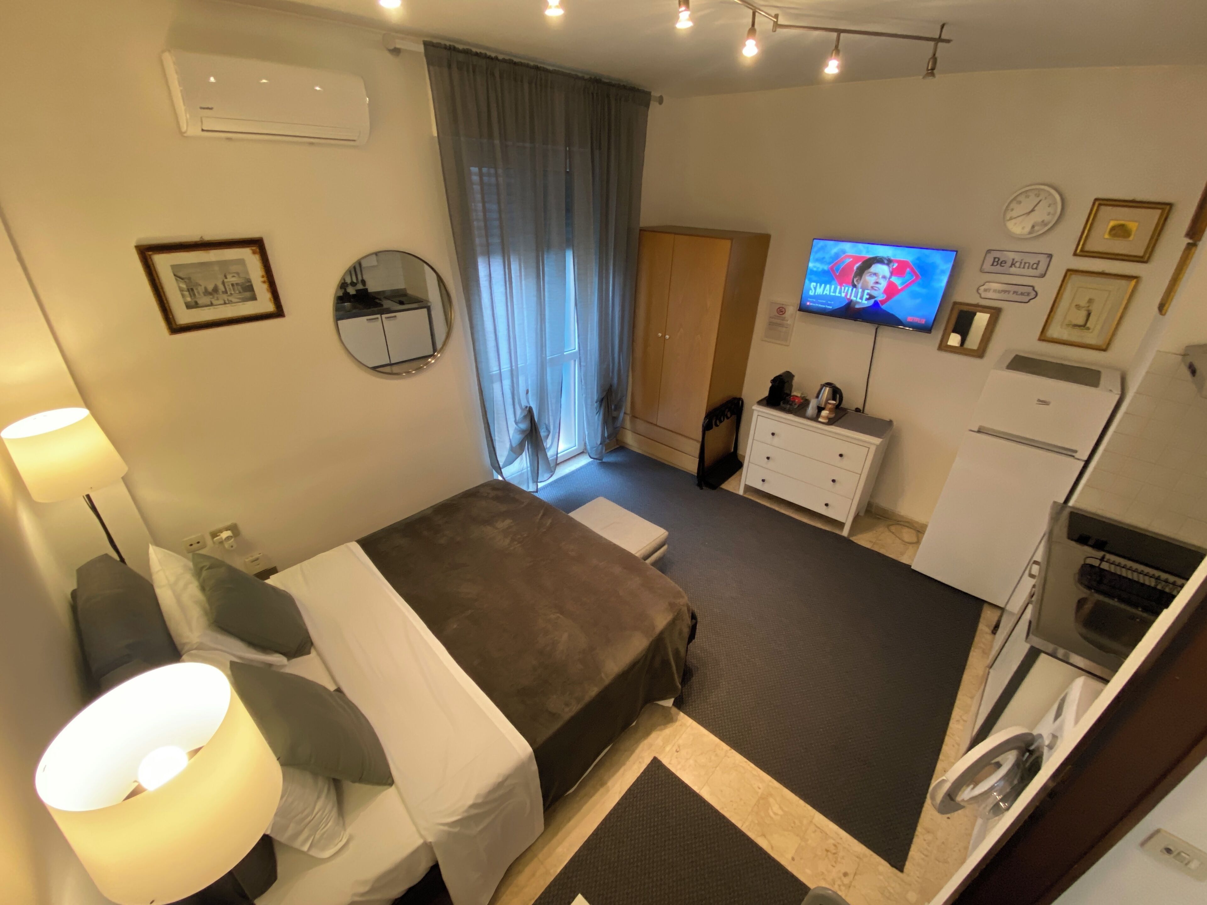 A hotel room with a bed, a desk, a chair, a TV, a wardrobe, a dresser, a mirror, and a refrigerator.
