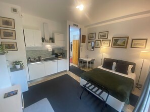 Una habitación de hotel compacta con kitchenette, una cama con manta verde, un escritorio y una silla.