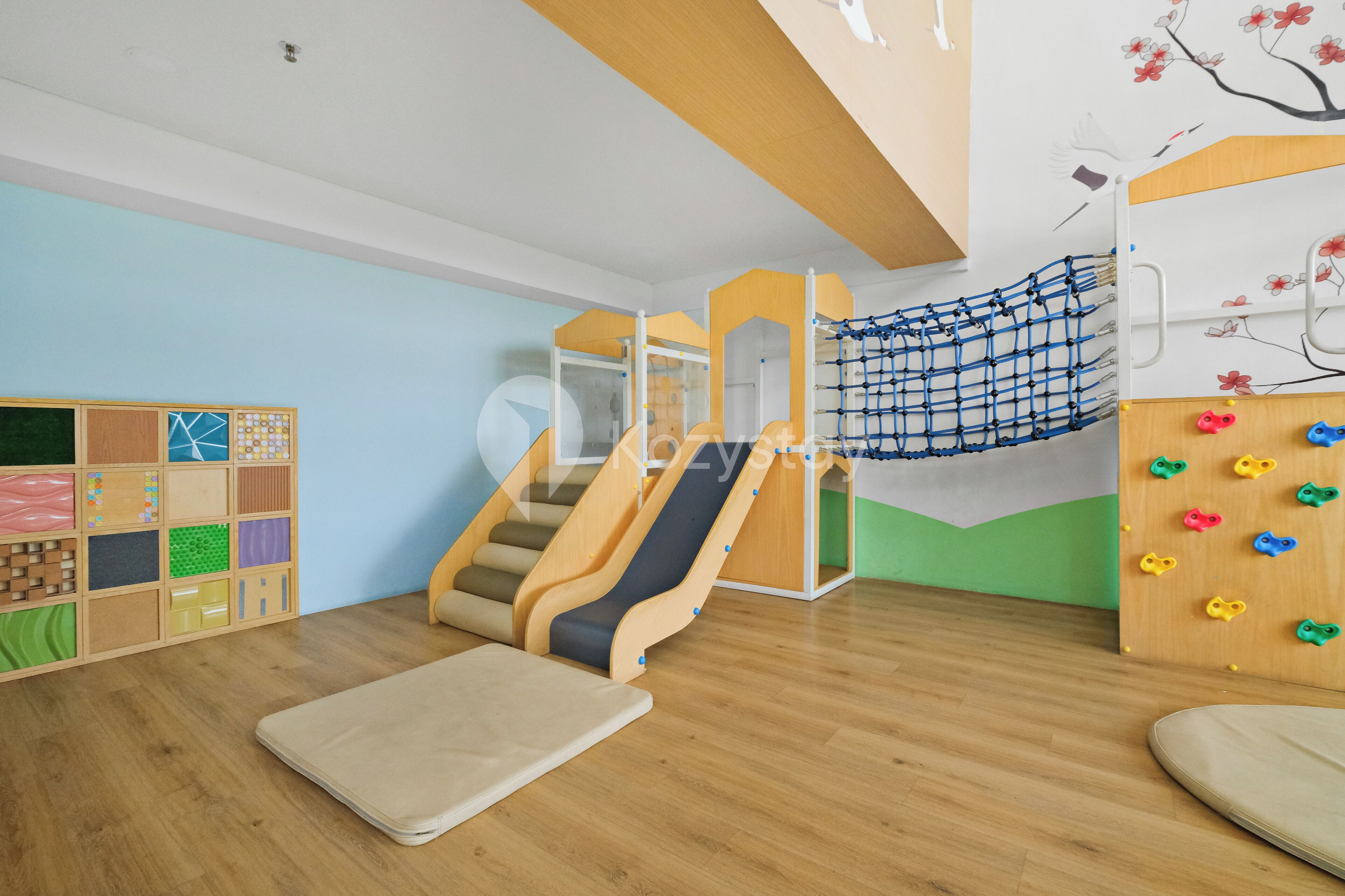 A children's play area with a slide, climbing net, and colorful climbing wall.