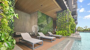 A modern outdoor pool area with lounge chairs, a wooden deck, and a vertical garden wall. - Minori by Kozystay - Alam Sutera (South Tangerang)