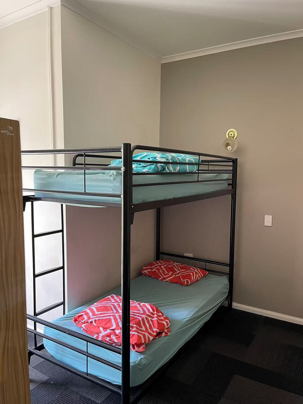 A bunk bed room with a door on the left, a light switch on the wall, and a lock on the door.