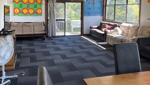 Una habitación amplia con un gran ventanal, ventilador de techo y piso alfombrado.