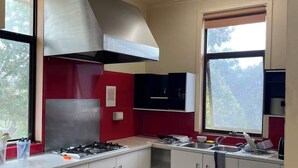 Cocina con alacenas blancas, extractor de acero inoxidable y ventana con vista a árboles.