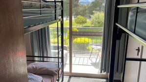 Habitación con literas, una puerta corrediza de vidrio que da a un espacio exterior con patio y vegetación.