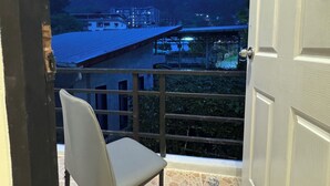 A balcony with a chair, a tiled floor, and a view of buildings and hills. - Chapter 26 Guesthouse (Patong)