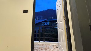 A doorway leading to a balcony with a view of buildings and a hill. - Chapter 26 Guesthouse (Patong)