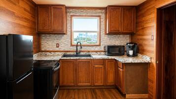 A compact kitchen with wooden cabinets, a black refrigerator, a microwave, and a coffee maker.