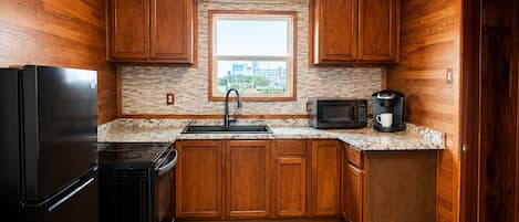 A compact kitchen with wooden cabinets, a black refrigerator, a microwave, and a coffee maker.