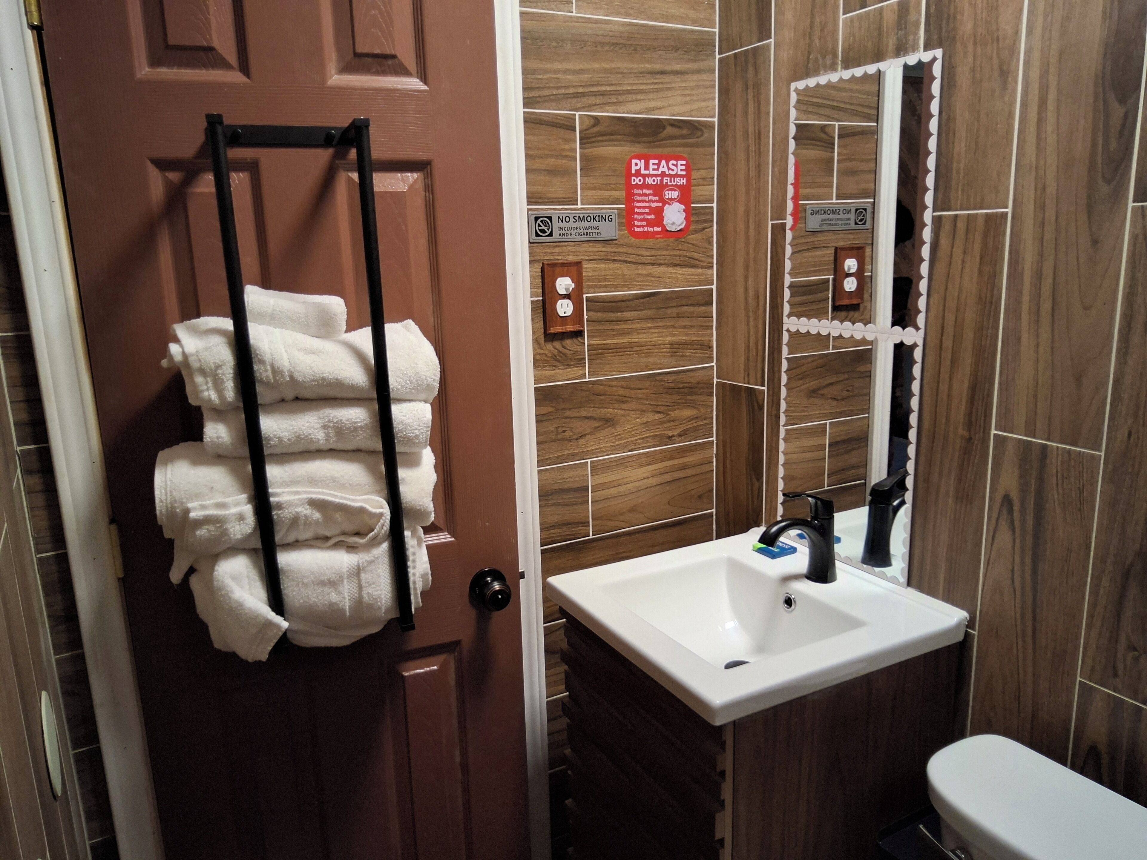 A bathroom with a wooden wall, a sink, a toilet, and a towel rack with folded towels.