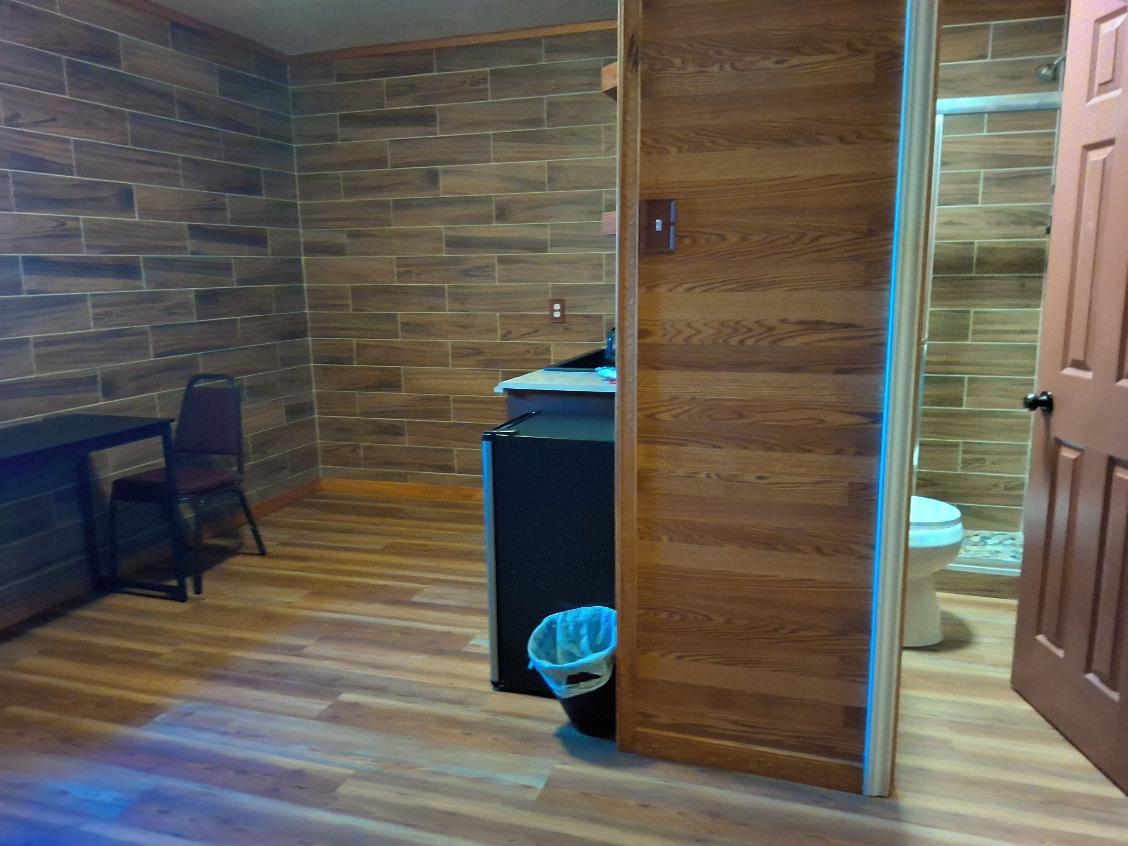 A room with a wooden floor, a desk with a chair, and a wooden wall.